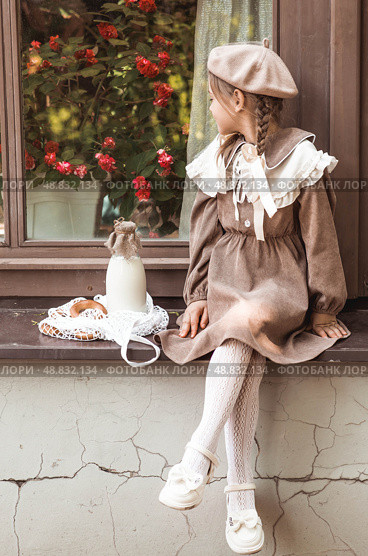 Vintage accessories and retro-style clothes. A small, beautiful girl with bows in her hair, in a beige dress and a beret outdoors with bagels and milk in a string bag. Стоковое фото, фотограф Photojuli / Фотобанк Лори