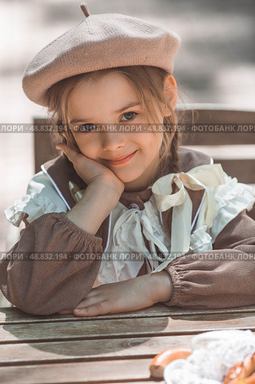 Vintage women's accessories and retro-style clothing. A small, beautiful girl with bows in her hair, in a beige dress and a beret outdoors. Стоковое фото, фотограф Photojuli / Фотобанк Лори