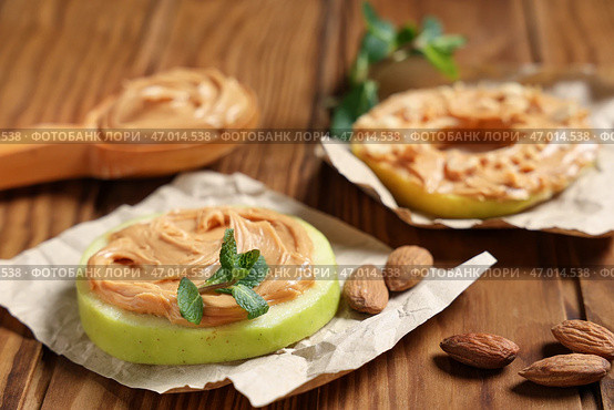Вкусные яблочные кружочки с ореховой пастой, мятными листьями и миндалем на деревянном фоне. Стоковое фото, фотограф Pixel_shot / Фотобанк Лори