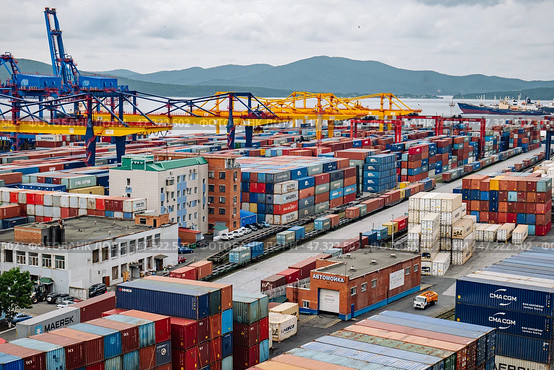 Vladivostok, Russia - August 9, 2021: Cargo cranes loading colorful containers in the port of vladivostok, russia, with the zolotoy rog bridge in the background. Редакционное фото, фотограф Mikhail Davidovich / Фотобанк Лори