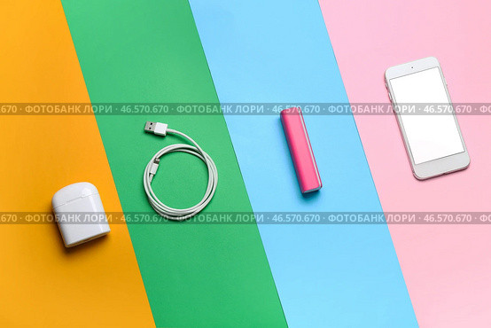 Внешний аккумулятор с мобильным телефоном, USB-кабелем и наушниками на цветном фоне. Стоковое фото, фотограф Pixel_shot / Фотобанк Лори