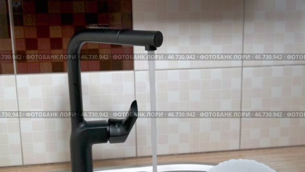 Водопроводная вода течет из открытого стильного черного крана на кухне. Крупный план. Оригинальный звук. Редакционное видео, видеограф Sergei Gorin / Фотобанк Лори