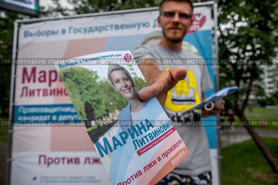 Волонтер предвыборного штаба Марины Литвинович, кандидата в депутаты в Государственную Думу РФ от партии "Яблоко", раздает агитационные листовки на фоне баннера в городе Москве, Россия (2021 год). Редакционное фото, фотограф Николай Винокуров / Фотобанк Лори