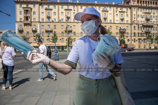 Волонтер раздает бесплатно медицинские маски людям на улице, которые пришли смотреть проход военной техники во время военного парада, посвященного 75-й годовщины Победы в Великой Отечественной войне, на Красной площади в городе Москве, Россия (2020 год). Редакционное фото, фотограф Николай Винокуров / Фотобанк Лори