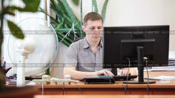 Вспотевший офисный сотрудник сидит под обдувающим вентилятором на рабочем месте перед экраном монитора. Стоковое видео, видеограф Кекяляйнен Андрей / Фотобанк Лори