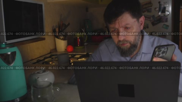 Взрослый мужчина, работая за ноутбуком, сравнивает данные на своем телефоне с экраном компьютера. Стоковое видео, видеограф Ярославский Максим / Фотобанк Лори