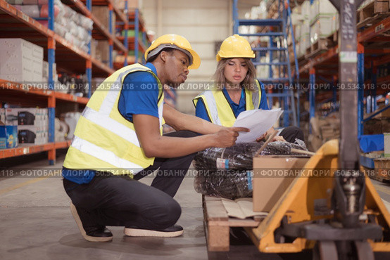 Warehouse workers inspect goods together on pallet trucks in a large warehouse. Стоковое фото, агентство Ingram Publishing / Фотобанк Лори