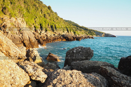 Waves gently crash against the rugged rocks while the sun sets over the horizon. Experience the serene beauty of this coastal location filled with natural wonders. Canj, Montenegro, Adriatic sea (2024 год). Стоковое фото, фотограф Юлия Петровская / Фотобанк Лори