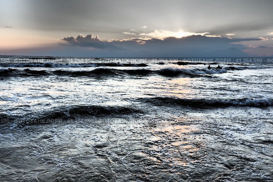 Waves with foam. Beautiful sunset. Foamy waves roll over the sandy shore. Vityazevo, Anapa, Black Sea. Tourist mecca, health resort. Colorful clouds in the evening sky. The rays reflect off the water. Стоковое фото, фотограф Юлия Петровская / Фотобанк Лори