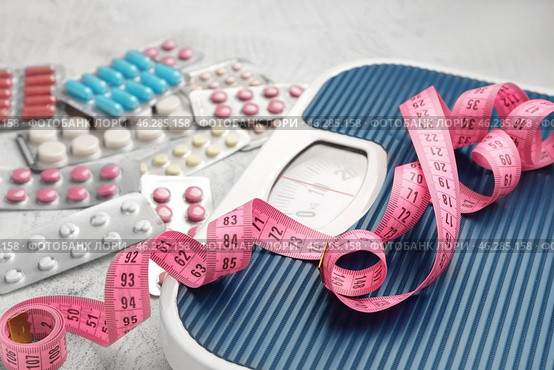 Weight loss pills, scales and measuring tape on grey background. Стоковое фото, фотограф Pixel_shot / Фотобанк Лори