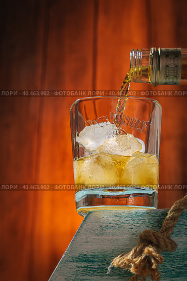 Whiskey from a bottle is poured into a glass with ice. Wooden background. Alcoholic drink. Moscow Russia March 27, 2022. Стоковое фото, фотограф Юрий Поздников / Фотобанк Лори