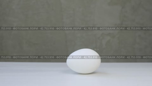 White chicken eggs roll and rotate on a white table. Food product on gray background. Стоковое видео, видеограф Дмитрий Кобзев / Фотобанк Лори
