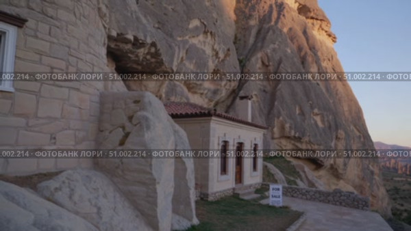 White stone house nestled against rocky cliff, featuring sale sign during golden sunset with mountainous landscape in Cappadocia, Turkey. Стоковое AI-видео, аниматор Данил Руденко / Фотобанк Лори