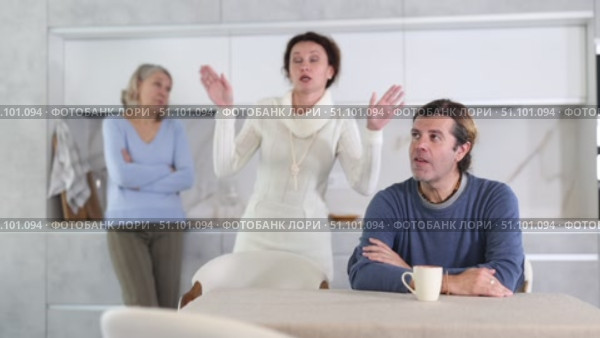 Wife and mother swear at man who puts up with it while sitting at kitchen table. Стоковое видео, видеограф Яков Филимонов / Фотобанк Лори