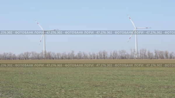 Wind turbines spin energetically against a blue sky, harnessing renewable energy in the countryside field on spring. Supporting farmers through innovative practices. Green and renewable power concept. Стоковое видео, видеограф Ирина Михайличенко / Фотобанк Лори