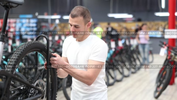 With keen attention, young buyer examining wheel and gear mechanism of bicycle in store to ensure that parts guaranteeing cycling safety. Стоковое видео, видеограф Яков Филимонов / Фотобанк Лори