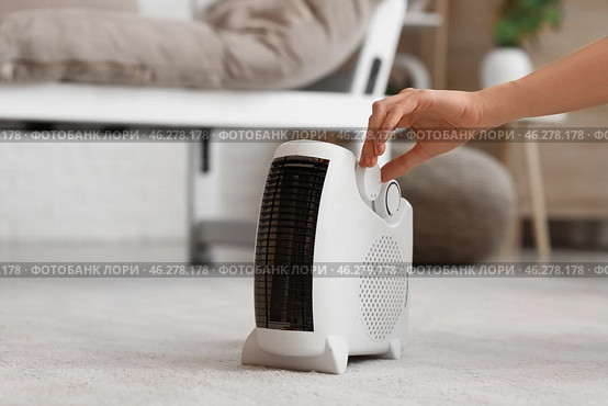 Woman adjusting electric fan heater in living room, closeup. Стоковое фото, фотограф Pixel_shot / Фотобанк Лори