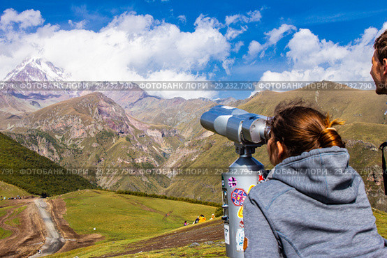 Woman and man looking in binoscope directed towards the snowy mountain tops of Kazbeg from the view point Gergeti Trinity Church Tsminda Sameba Holy Church near the village of Gergeti in Georgia (2018 год). Редакционное фото, фотограф Алексей Ширманов / Фотобанк Лори