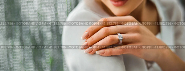 Woman Flaunting Her Elegant Diamond Engagement Ring. Close-up of a woman's hand as she shows off a sparkling diamond ring, symbolizing engagement. Стоковое AI-изображение, AI-художник Igor Tichonow / Фотобанк Лори
