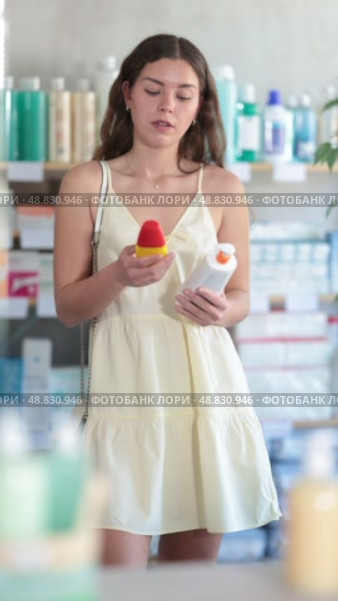 Woman in a summer dress stands near the counter in a pharmacy and chooses a sunscreen and SPF to protect the skin. Стоковое видео, видеограф Яков Филимонов / Фотобанк Лори