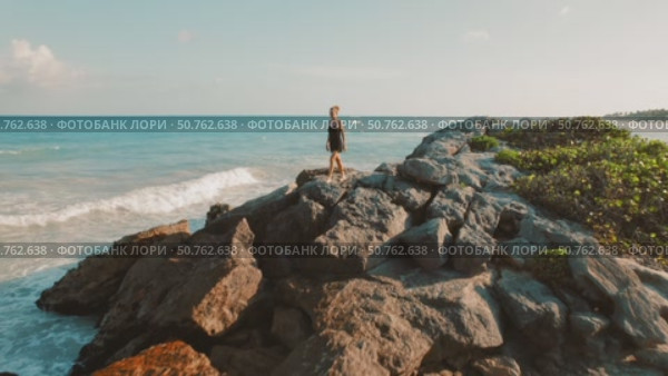 Woman in black walking on rocky coastline by the Caribbean Sea in Tulum Mexico. Стоковое видео, видеограф Igor Tichonow / Фотобанк Лори