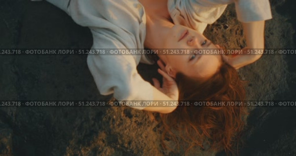 Woman lying on black volcanic rocks in relaxed pose with soft golden sunlight. Стоковое видео, видеограф Ольга Сухарева / Фотобанк Лори