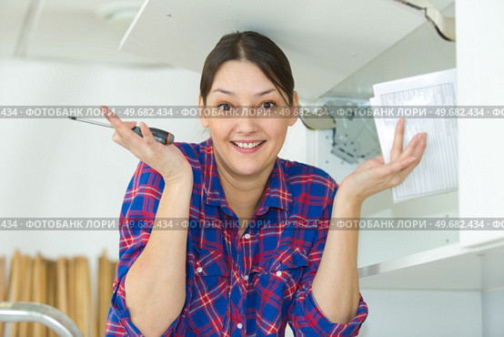 woman making clueless hand gesture while fitting kitchen cupboard. Стоковое фото, агентство Ingram Publishing / Фотобанк Лори