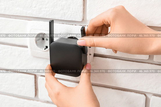 Woman plugging black WiFi repeater in electric socket on white brick wall. Стоковое фото, фотограф Pixel_shot / Фотобанк Лори