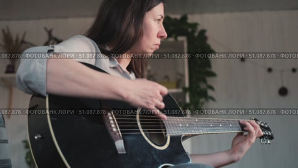 Woman Practicing Guitar in Cozy Room at Home. Strumming black acoustic guitar. Female learning to play music. Person hand on a guitar neck. Guitarist working on melody, performance, practice indoors. Стоковое видео, видеограф Марина Демидюк / Фотобанк Лори