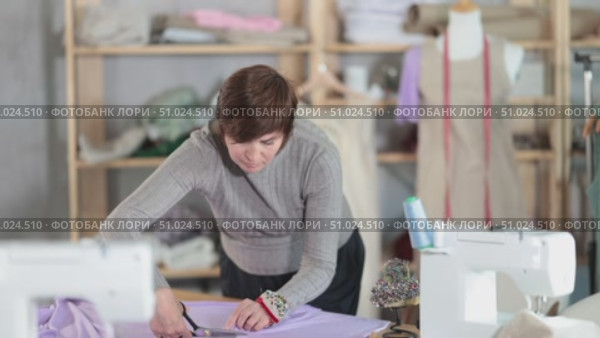 Woman seamstress cuts fabric on cutting table. Стоковое видео, видеограф Яков Филимонов / Фотобанк Лори