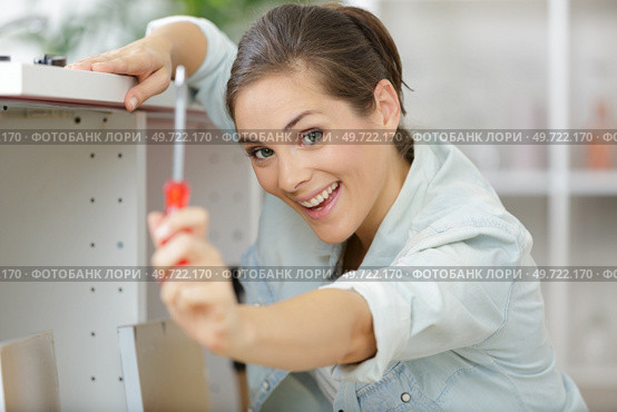 woman showing screwdriver she is using to assemble cupboard. Стоковое фото, агентство Ingram Publishing / Фотобанк Лори
