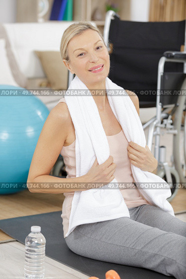 woman sits next to a wheelchair on blue yoga mat. Стоковое фото, агентство Ingram Publishing / Фотобанк Лори