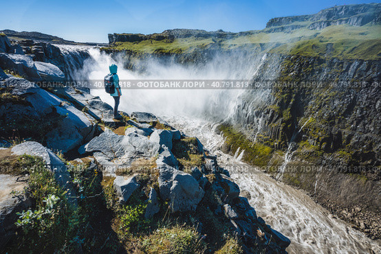 Woman traveler at cliff edge Dettifoss waterfall in Northeast Iceland. Dettifoss is a waterfall in Vatnajokull National Park reputed to be the most powerful waterfall in Europe. Стоковое фото, фотограф Igor Tichonow / Фотобанк Лори