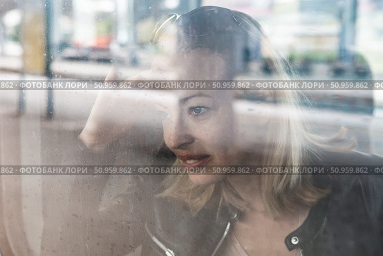 Woman traveler contemplating outdoor view from window of train. Young lady on commute travel to work sitting in bus or train. Стоковое фото, фотограф Matej Kastelic / Фотобанк Лори