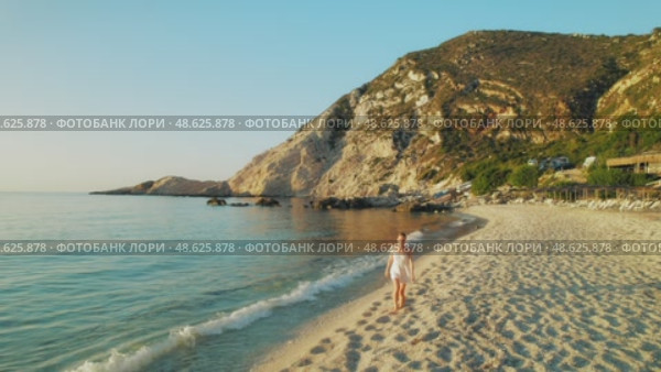 Woman walking barefoot on a quiet sandy beach in Kefalonia during the warm evening light. Стоковое видео, видеограф Igor Tichonow / Фотобанк Лори