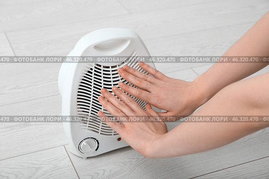 Woman warming near electric fan heater at home, closeup. Стоковое фото, фотограф Pixel_shot / Фотобанк Лори