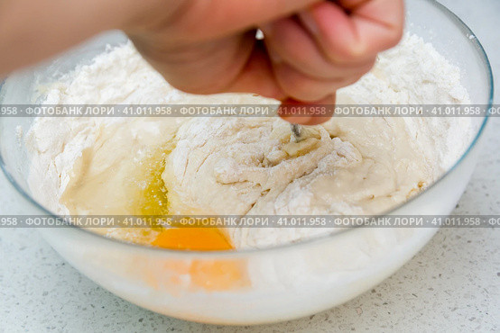 Woman's hands with an yeast dough. The woman has added the yolk of a chicken egg and is stirring the baking dough in a glass bowl. Женские руки с дрожжевым тестом. Женщина добавила желток куриного яйца и замешивает тесто для выпечки в стеклянной миске. Стоковое фото, фотограф Дмитрий Березнев / Фотобанк Лори
