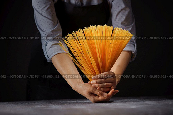 Woman’s hands with gluten free spaghetti made from rice and maize over a wooden table on a black background. Mediterranean healthy diet. Fresh italian uncooked homemade pasta in female hands over a wooden table. Стоковое фото, агентство Ingram Publishing / Фотобанк Лори