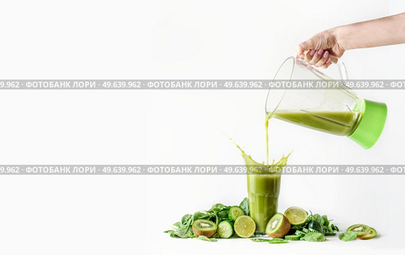 Women hand pouring green smoothie from blender in glass with splashing and ingredients: kiwi, cucumber, lime and spinach at white background. Healthy lifestyle, dieting and detox food. Стоковое фото, агентство Ingram Publishing / Фотобанк Лори