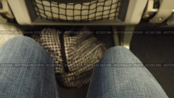 Women's legs in denim pants in a narrow gap between seats on an airplane. Economy class for air travel. A woman moves her legs to avoid blood clots and varicose veins. Travel, flights and business. Стоковое видео, видеограф Юлия Петровская / Фотобанк Лори