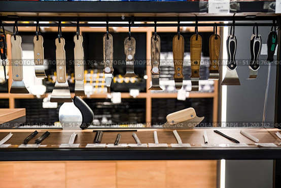 Wooden and plastic handled spatula tools hanging on display in a hardware store, used for stretch ceiling installation and PVC film fitting. Стоковое фото, фотограф Татьяна Терехина / Фотобанк Лори
