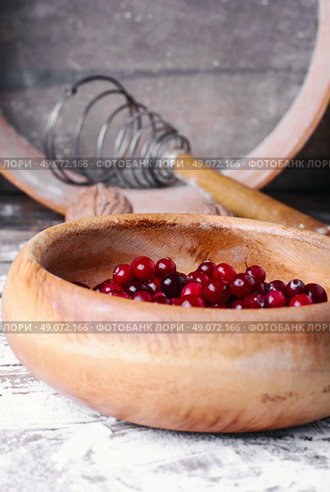Wooden bowl with cranberries on a wooden background with kitchen smeared with flour. Ripe cranberries in bowls. Стоковое фото, агентство Ingram Publishing / Фотобанк Лори