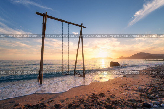 Wooden swing in beautiful blue sea with waves, sandy beach, sky with golden sunlight at sunset in summer. Vacation in Oludeniz, Turkey. Tropical landscape with swing on sea coast, water. Travel. Стоковое фото, агентство Ingram Publishing / Фотобанк Лори