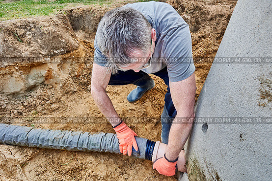 Worker connects perforated drain pipe to septic tank through which wastewater flows into leach field. Стоковое фото, фотограф Владимир Григорьев / Фотобанк Лори