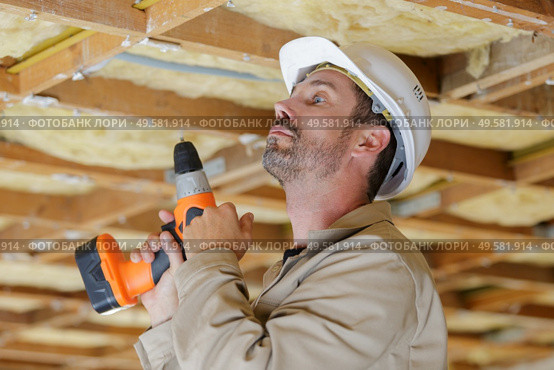 workman holding cordless drill looking up at roof timbers. Стоковое фото, агентство Ingram Publishing / Фотобанк Лори