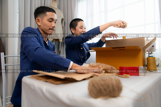 Young Asian businessman and woman Clothes are being packaged for delivery to customers in cardboard boxes and cushioned lump from natural materials that are not toxic to the planet. Стоковое фото, агентство Ingram Publishing / Фотобанк Лори