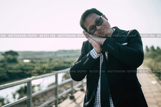 Young Asian Businessman wearing suit with tie and glasses close his eyes with tired and sleeping for relaxing at outdoors. Стоковое фото, агентство Ingram Publishing / Фотобанк Лори