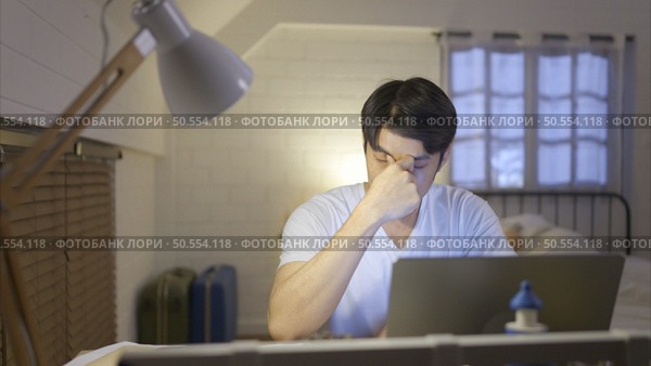 Young Asian man working overtime at home take medicine and drink water to relieve stress and headaches. Стоковое фото, агентство Ingram Publishing / Фотобанк Лори