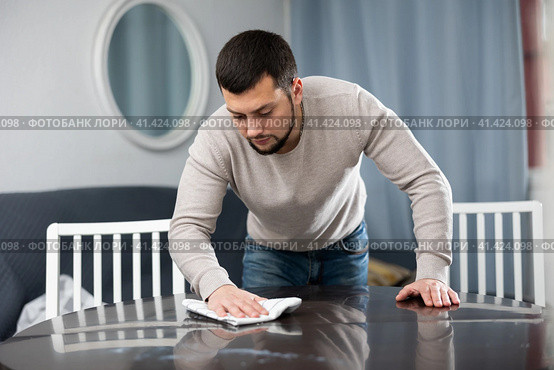 Young bachelor wiping surface of dining table in apartment. Стоковое фото, фотограф Яков Филимонов / Фотобанк Лори