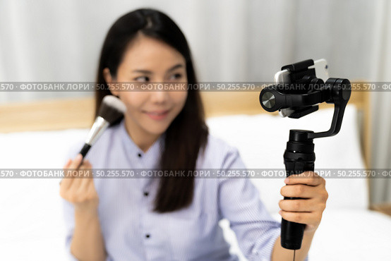 Young beautiful Asian woman beauty vlogger or blogger recording live how to make up tutorial to share on social media using Gimbal Stabilizer on mobile phone. Using for vlog social media influencer concept. Focus on Stabilizer. Стоковое фото, агентство Ingram Publishing / Фотобанк Лори